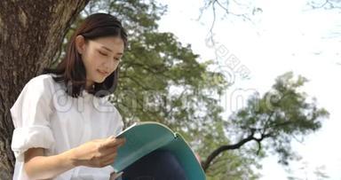 年轻迷人的亚洲女人坐在草地上的一个夏天的公园里，在日落时看书。